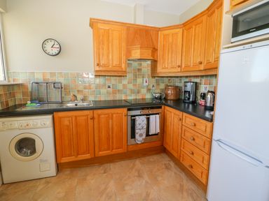 A kitchen with wooden cabinets a washing machine a stainless steel oven fridge microwave and various kitchen appliances at Sea View Hideaway in Lahinch County Clare