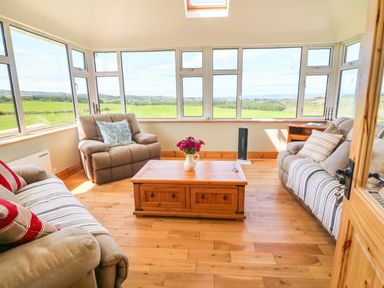 A sunroom with two sofas and one armchair around a wooden coffee table with flowers at Sea View Hideaway in Lahinch County Clare