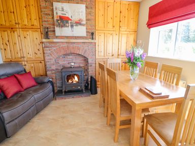 A dining room with a wooden table and chairs a leather sofa a brick fireplace and wooden cabinets at Sea View Hideaway in Lahinch County Clare