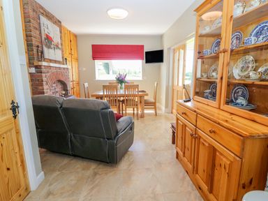 A dining area with wooden table and chairs a black leather sofa a brick fireplace and a wooden cabinet with china at Sea View Hideaway in Lahinch County Clare