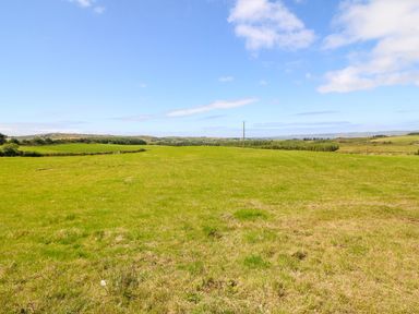 A grassy field with hills and trees in the distance under a blue sky at Sea View Hideaway in Lahinch County Clare