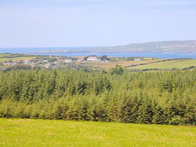 A landscape with green fields trees houses and sea in the background at Sea View Hideaway in Lahinch County Clare