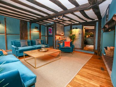 A living room with blue sofas and armchairs a wooden coffee table and exposed wooden beams at 3 Masons Court Stratford-Upon-Avon