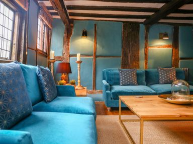 A living room with blue sofas wooden beams on walls and ceiling and a wooden coffee table at 3 Masons Court Stratford-Upon-Avon