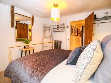 A bedroom with a bed covered by a quilt and pillows next to a wooden door and a small table with a plant at 3 Masons Court in Stratford-Upon-Avon