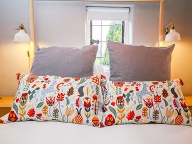 A bed with two large gray pillows and two smaller pillows with colorful floral patterns at 3 Masons Court in Stratford-Upon-Avon