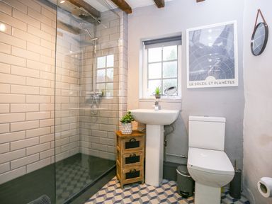 A bathroom with a walk-in shower sink toilet small wooden cabinet and window at 3 Masons Court Stratford-Upon-Avon
