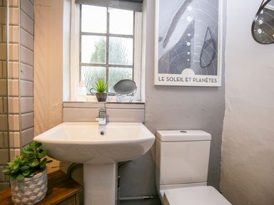 A bathroom with a pedestal sink toilet plants and a window with a space-themed poster on the wall at 3 Masons Court in Stratford-Upon-Avon