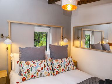A bedroom with a bed with floral pillows wooden headboard wall lamps and a window at 3 Masons Court in Stratford-Upon-Avon
