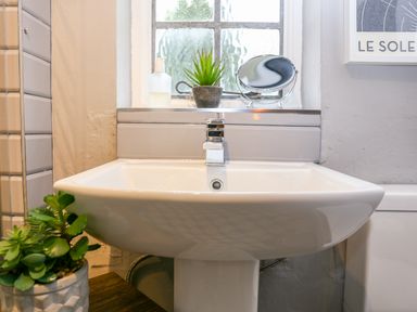 A bathroom sink with a chrome faucet and potted plants on the windowsill at 3 Masons Court in Stratford-Upon-Avon