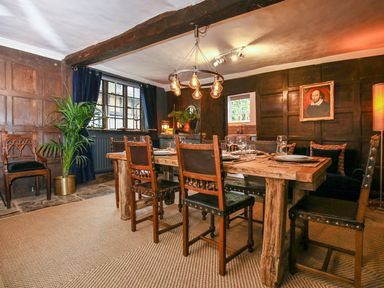 A dining room with a wooden table and chairs with a plant and a framed painting on the wall at 3 Masons Court in Stratford-Upon-Avon