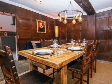 A dining room with a wooden table set for six and dark wooden paneled walls at 3 Masons Court in Stratford-Upon-Avon