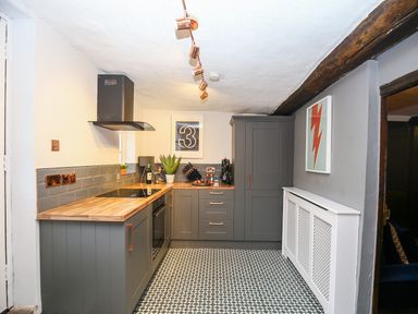 A kitchen with gray cabinets wooden countertops a black oven and stove a plant and framed pictures on the walls at 3 Masons Court in Stratford-Upon-Avon