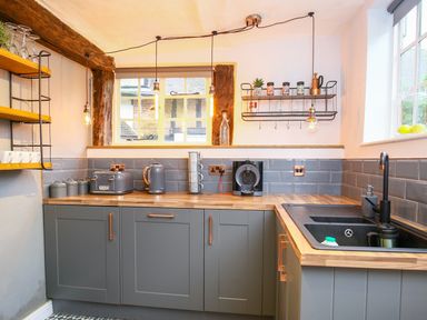 A kitchen with grey cabinets wooden countertops a black sink hanging shelves and a window at 3 Masons Court Stratford-Upon-Avon