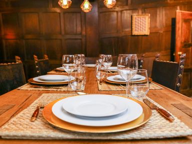 A wooden dining table set with plates wine glasses and cutlery in a room with wooden paneled walls at 3 Masons Court in Stratford-Upon-Avon