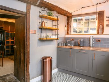 A kitchen with grey cabinets wooden countertops a copper trash can and hanging shelves at 3 Masons Court Stratford-Upon-Avon