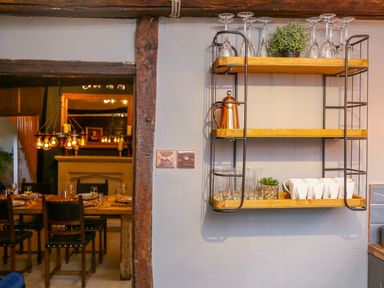 A wall-mounted shelf with glassware, mugs, a kettle and plants beside a dining room at 3 Masons Court Stratford-Upon-Avon