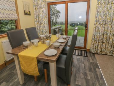 A dining table with four chairs set with dishes and a yellow table runner near a glass door with a view of green fields at Nicky Nook Lodge in Scorton
