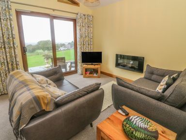 A living room with two sofas a television and sliding glass doors leading to a patio at Nicky Nook Lodge in Scorton
