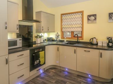 A kitchen with cream cabinets black countertop microwave oven utensils and a window with chevron patterned blind at Nicky Nook Lodge in Scorton