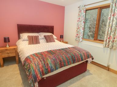 A bedroom with a double bed two bedside tables two lamps a window with floral curtains at Nicky Nook Lodge in Scorton