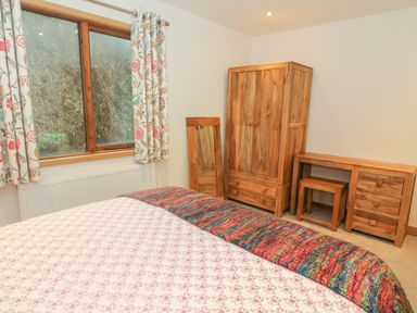 A bedroom with a bed a window with floral curtains a wooden wardrobe a wooden dresser and a full length mirror at Nicky Nook Lodge in Scorton