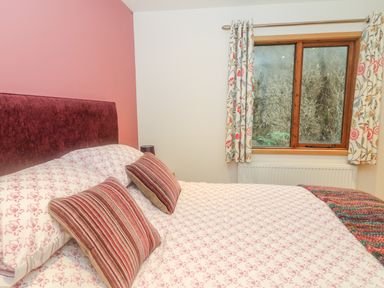 A bedroom with a bed and striped pillows next to a window with floral curtains at Nicky Nook Lodge in Scorton