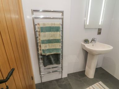 A bathroom with a wooden door a heated towel rail with towels a pedestal sink a mirror with lights and toiletries at Nicky Nook Lodge in Scorton