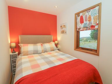 A bedroom with a bed and bedside tables with lamps and a window with patterned curtains at Nicky Nook Lodge in Scorton