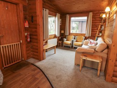 A sitting room with armchairs sofa wooden tables and windows in a wooden cabin at Glanton in Longframlington