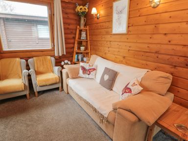 A living room with a beige sofa and two armchairs next to a wooden wall with a window and shelf at Glanton in Longframlington