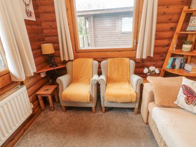 Two armchairs with yellow throws next to a beige sofa in a wooden cabin living room at Glanton in Longframlington