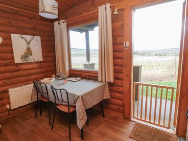A dining area with a table covered by a polka dot tablecloth and three chairs near a window and a door with a safety gate at Glanton in Longframlington