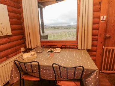 A dining table with a polka dot tablecloth and chairs near a window with curtains in a wooden room at Glanton in Longframlington
