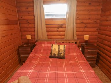 A bedroom with a bed covered by a red plaid blanket and two bedside tables with lamps at Glanton in Longframlington