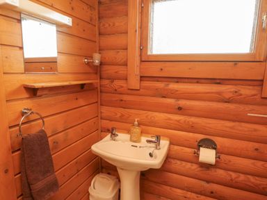 A bathroom with wooden walls a white sink with soap a towel hanging on a ring and a window at Glanton in Longframlington