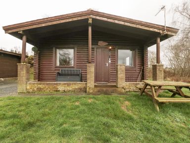 A wooden cabin with a covered porch a bench two windows a door and a picnic table on grass at Glanton in Longframlington