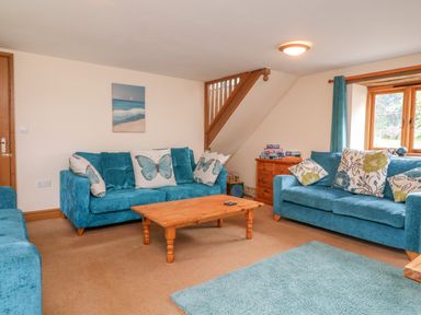 A living room with blue sofas floral and butterfly cushions wooden coffee table and wooden chest of drawers at The Shippon in Barnstaple