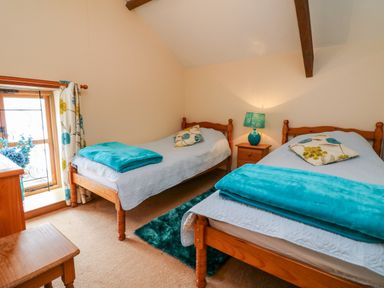 A bedroom with two single beds a bedside table with a lamp and a window with floral curtains at The Shippon in Barnstaple