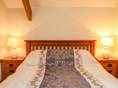 A bedroom with a wooden bed frame lamps on wooden bedside tables and a patterned bedspread at The Shippon in Barnstaple