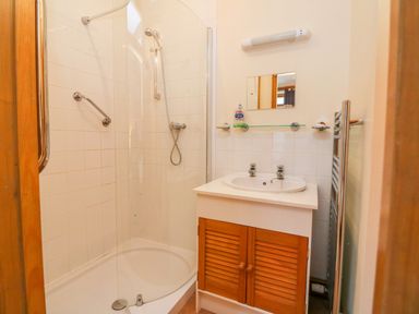 A bathroom with a shower enclosure a sink with wooden cabinet and a mirror at The Shippon in Barnstaple