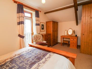 A bedroom with a wooden bed a floral armchair a wooden wardrobe a dresser and a vanity table with mirrors at The Shippon in Barnstaple