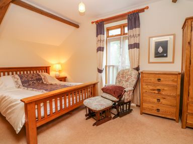 A bedroom with a wooden bed bedside table armchair with ottoman chest of drawers and wardrobe at The Shippon in Barnstaple
