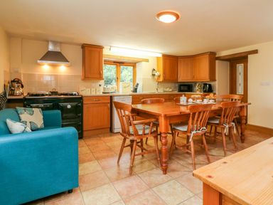 A kitchen with wooden cabinets a dining table with chairs and a blue sofa at The Shippon in Barnstaple