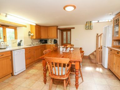 A kitchen with wooden cabinets a dining table and chairs and a staircase at The Shippon in Barnstaple