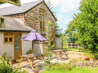 A stone cottage with wooden picnic tables and a purple umbrella in a garden at The Shippon in Barnstaple