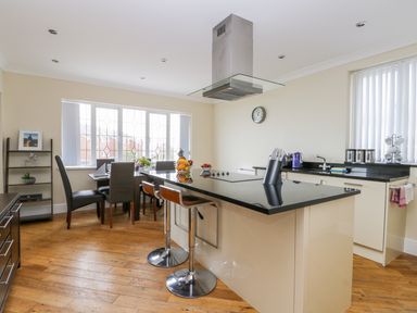 A kitchen with a black countertop island, bar stools, dining table, chairs, and a window at The Gansey Girl in Bridlington
