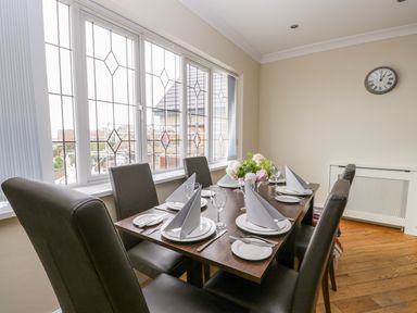 A dining room with a wooden table set with plates glasses and napkins and leather chairs next to windows at The Gansey Girl in Bridlington