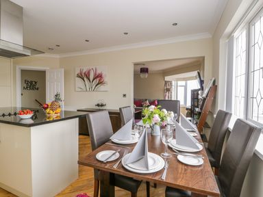 A dining room with a wooden table set with plates and napkins and an adjacent kitchen counter with fruit at The Gansey Girl in Bridlington