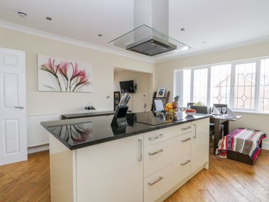 A kitchen with a black countertop island and knives set a dining table with chairs and a colorful blanket on a bench at The Gansey Girl in Bridlington